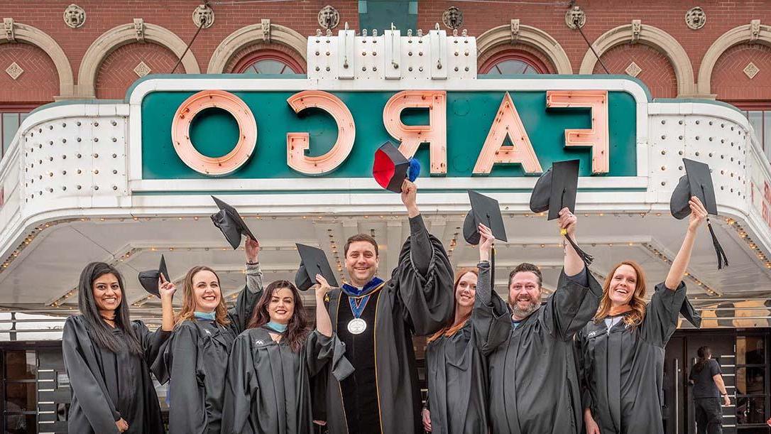 法戈大学的成年学生穿着毕业礼服站在法戈剧院外，与MG冰球突破试玩校长谢伊一起挥舞着毕业帽